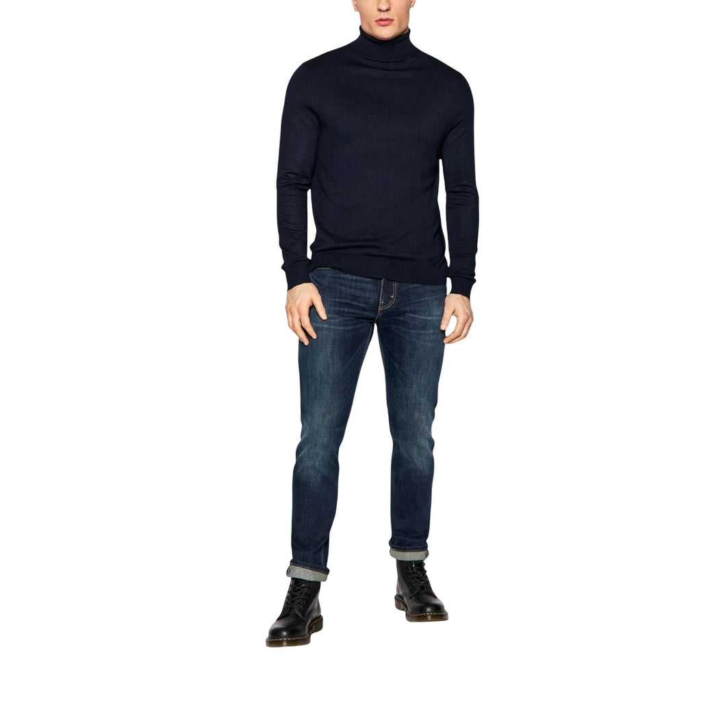 Person wearing a black turtleneck sweater and blue jeans on a white background